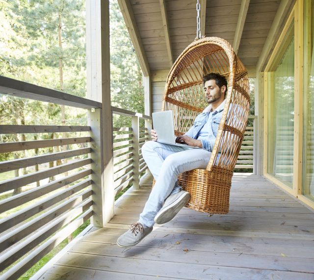 Mann sitzt entspannt mit Laptop auf einem Korbstuhl